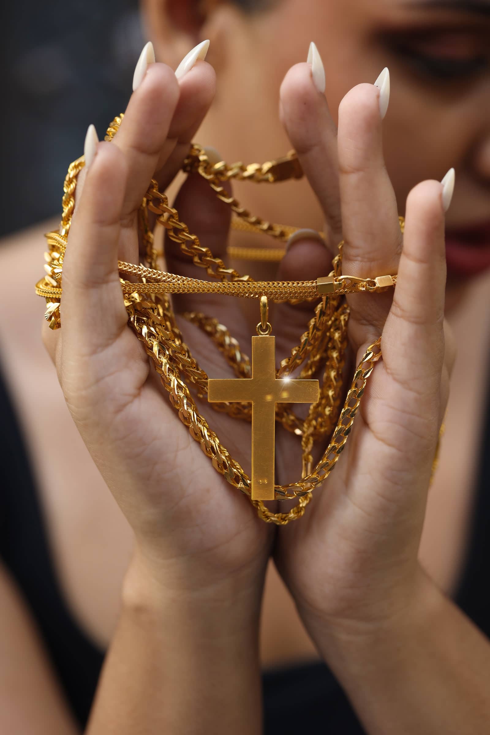 Heavy gold chains and a gold cross pendant held in cupped hands