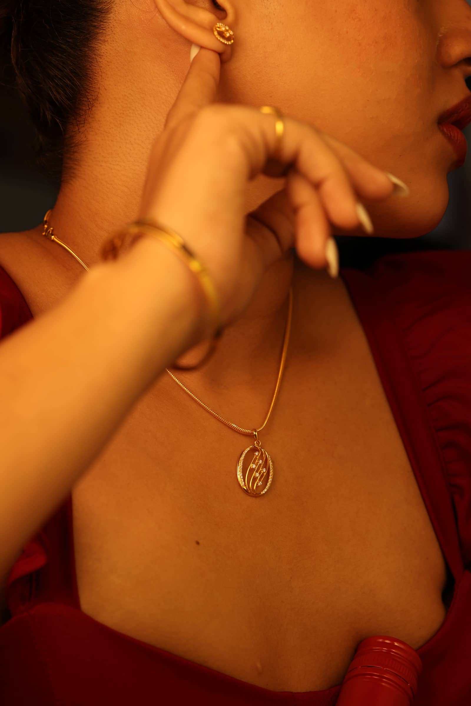 Gold pendant necklace, stud earring and bangle worn together