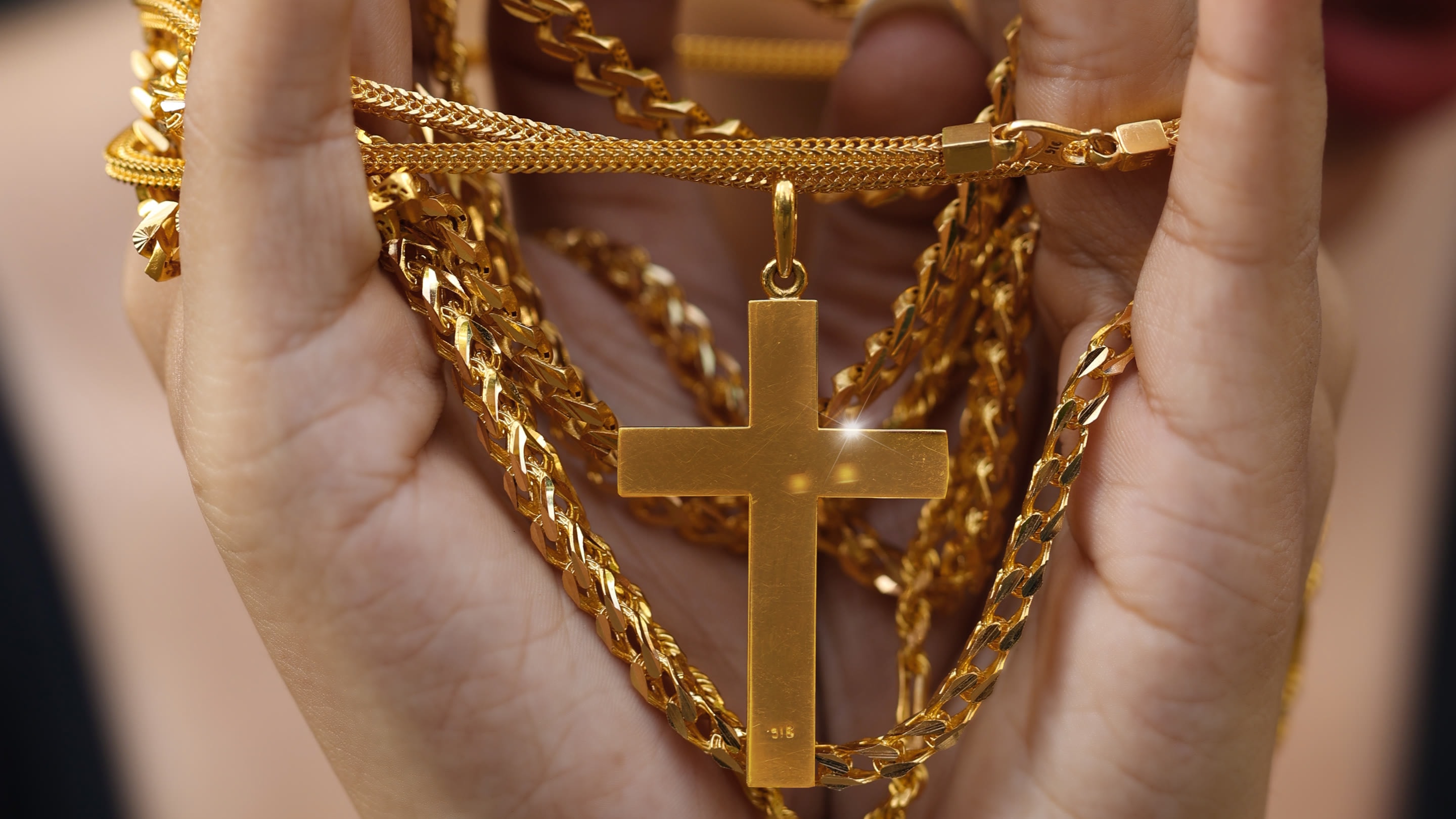 Gold chains and a polished gold cross pendant held in cupped hands